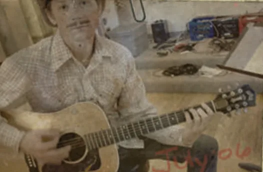 Phil Bunkum in a cowboy hat and western shirt playing an acoustic guitar